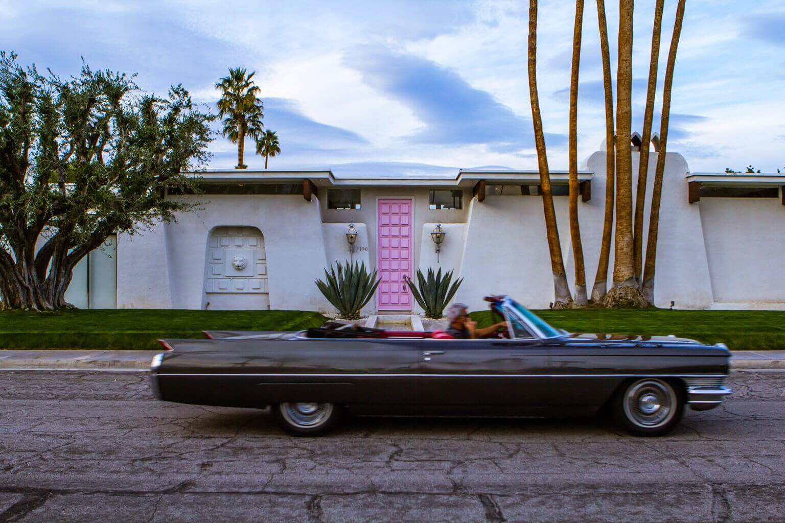 Man driving a classic car past the pink door house in Palm Springs California