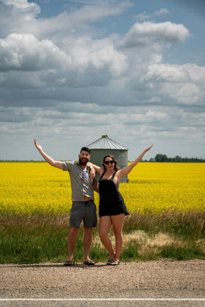Megan and Scott taking a photo along the road in Saskatchewan with yellow canola fields