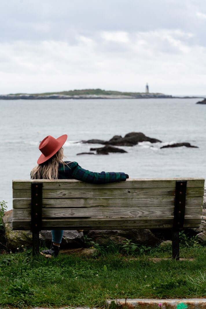 Megan enjoying the view of a lighthouse in the distance from a bench on Peaks Island in Portland Maine