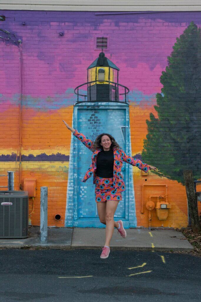 Megan jumping in front of the Concord Point Lighthouse mural in Havre de Grace Maryland