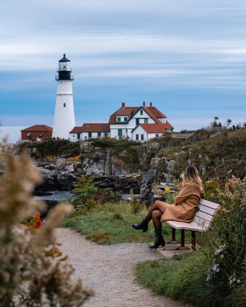 Megan sitting on a bench in Fort Williams Park taking in the view of Portland Head Lighthouse in Portland Maine