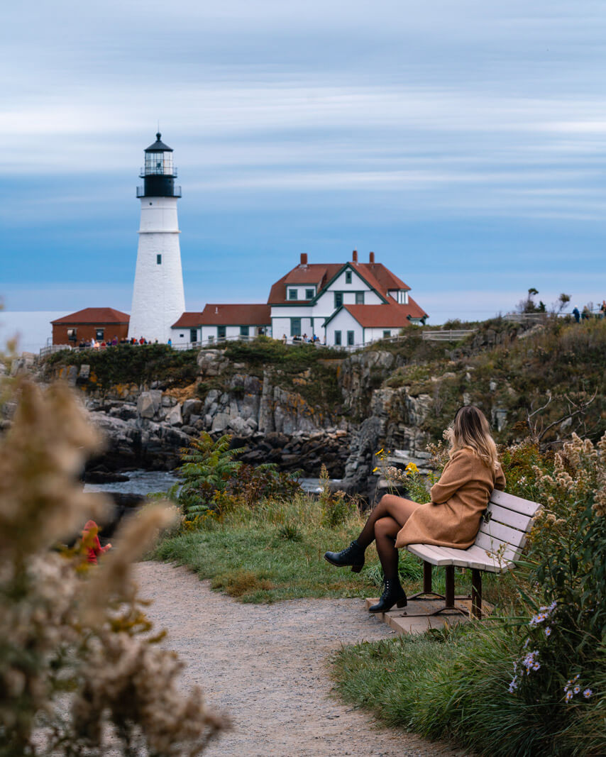 Megan sitting on a bench in Fort Williams Park taking in the view of Portland Head Lighthouse in Portland Maine
