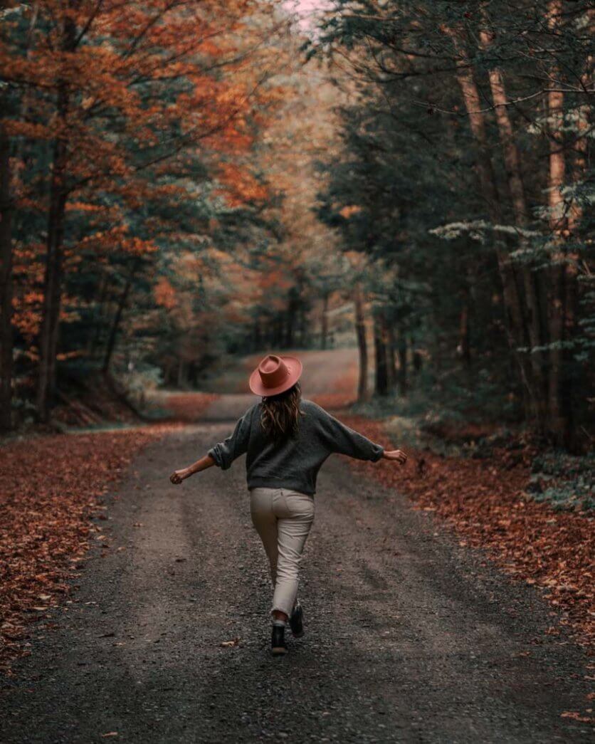 Megan wearing a pink hat in the fall walking down a remote road in the finger lakes