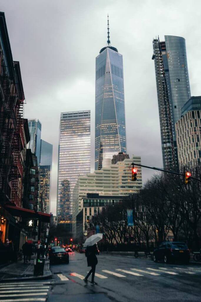 view of woman walking on a rainy day in Lower Manhattan with One World Trade Center in the background 