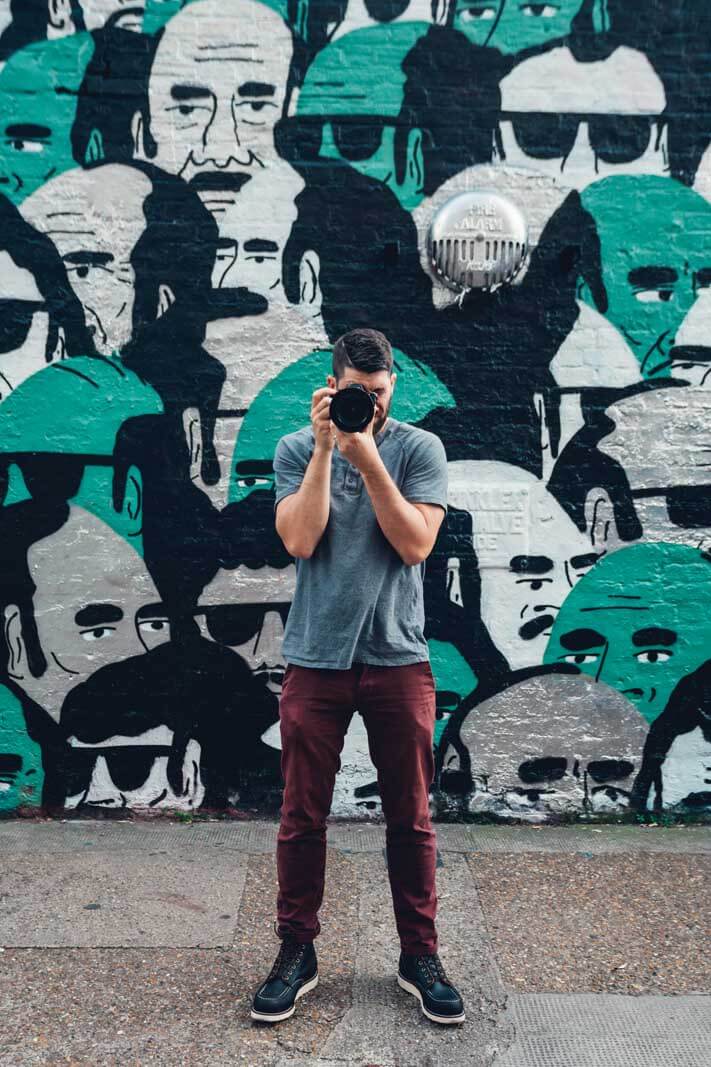 Scott taking a photo in front of a mural wall in East London