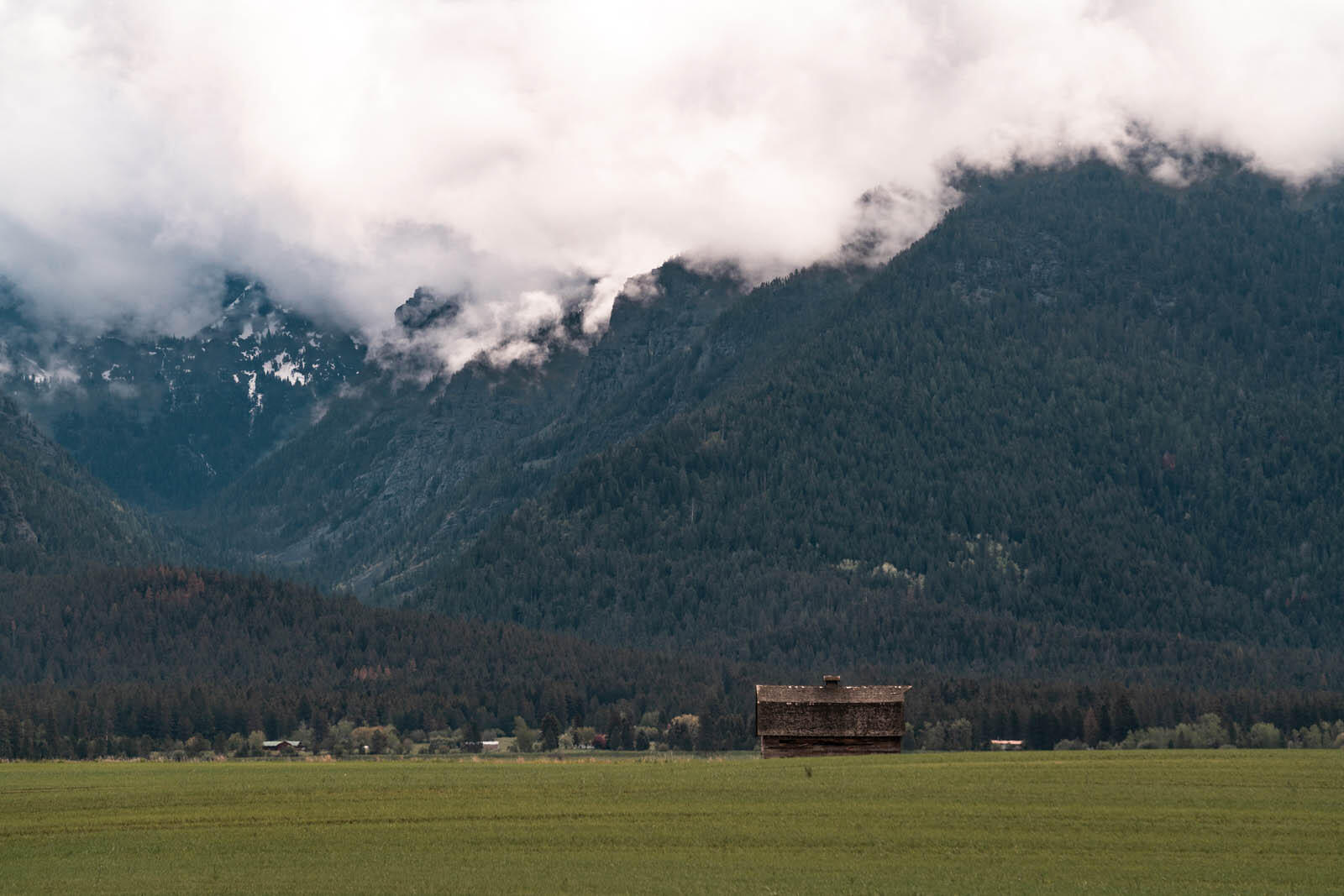 barn in a field along the roadside in Western Montana with clouds covering the mountains in the backdrop