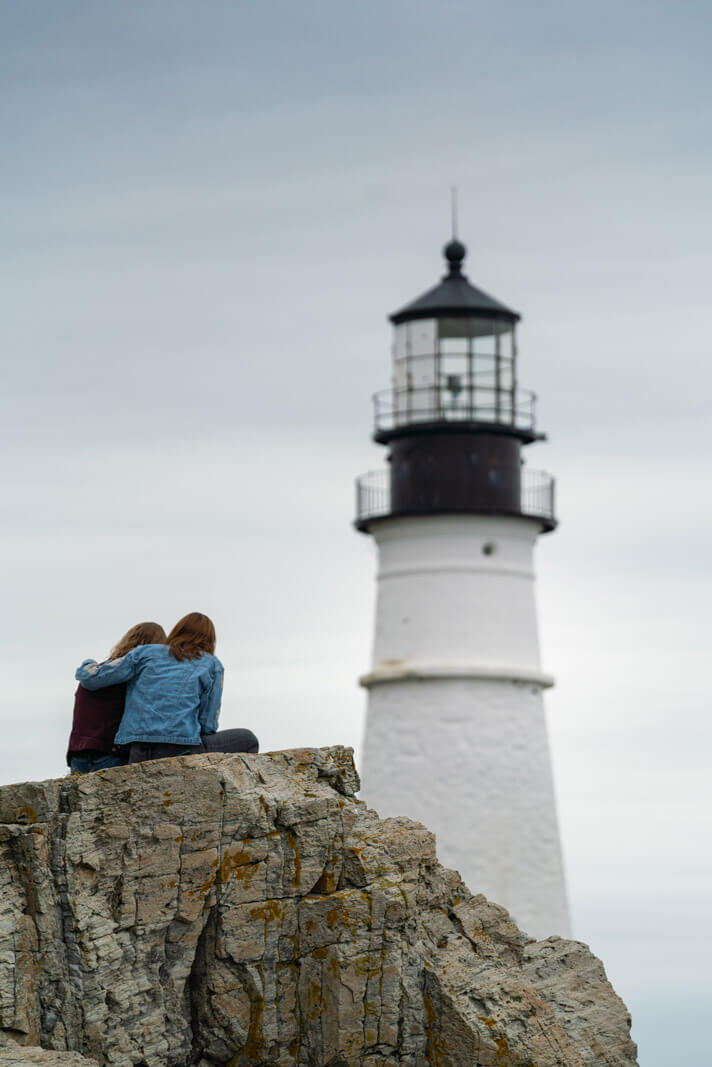 couple enjoying the view from a rock of Portland Head Lighthouse in Maine