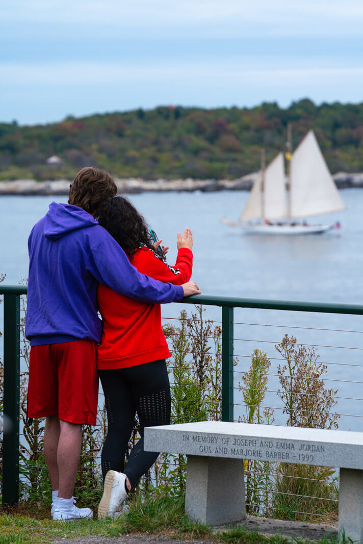 couple looking at a tall ship from Fort Wiliams Park at Portland Head Light in Maine