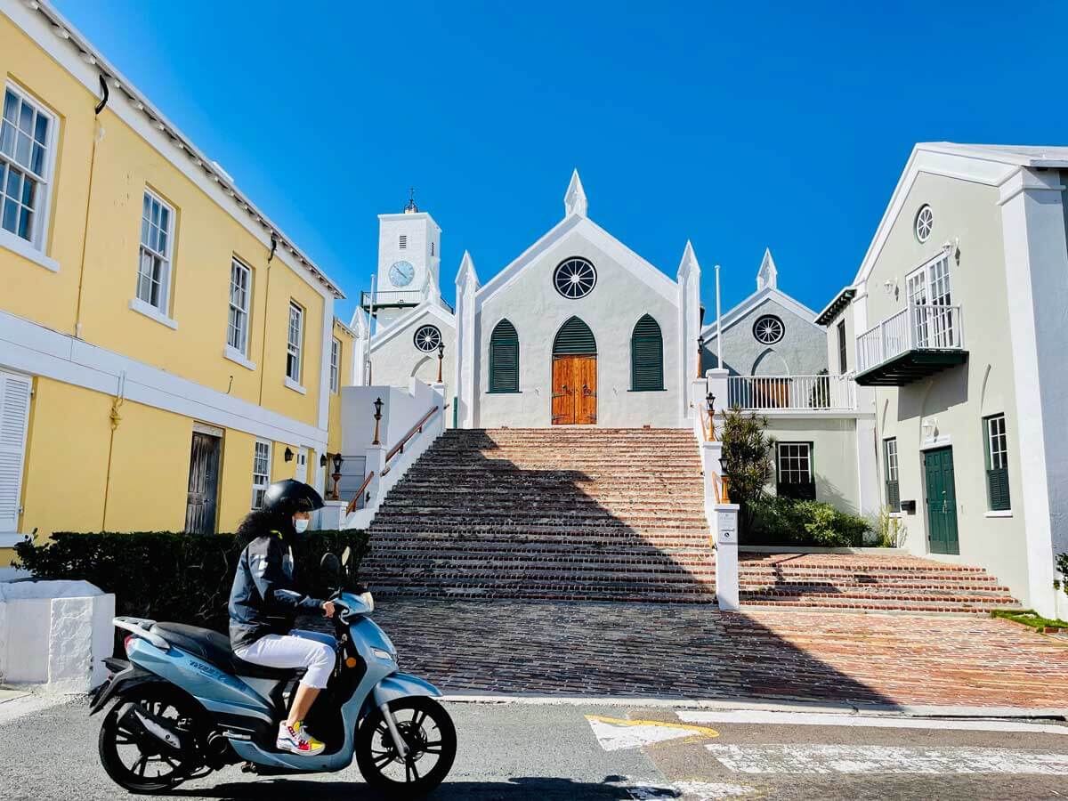 woman-driving-a-scooter-in-St-Georges-Bermuda-in-front-of-the-church